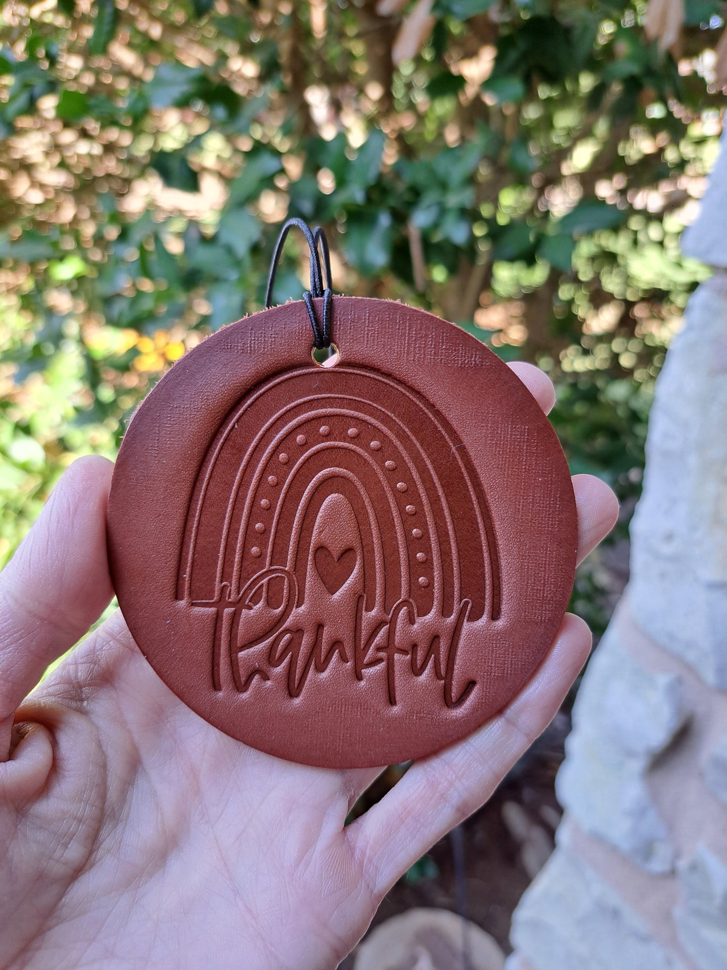 hand holdng a round leather air freshener with an embossed rainbow that says Thankful