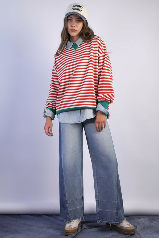 Person wearing a striped shirt, jeans, and a cap on a plain background