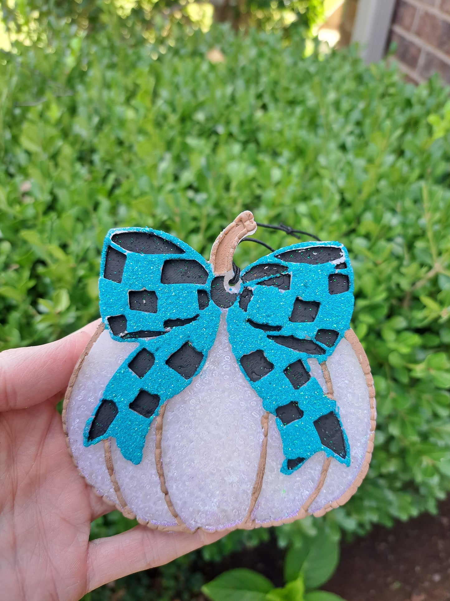 white pumpkin freshie with blue and black checkered bow held in a hand on a green background
