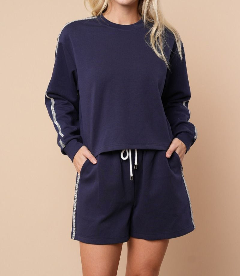 Woman wearing a navy blue sweatshirt and shorts set on a beige background
