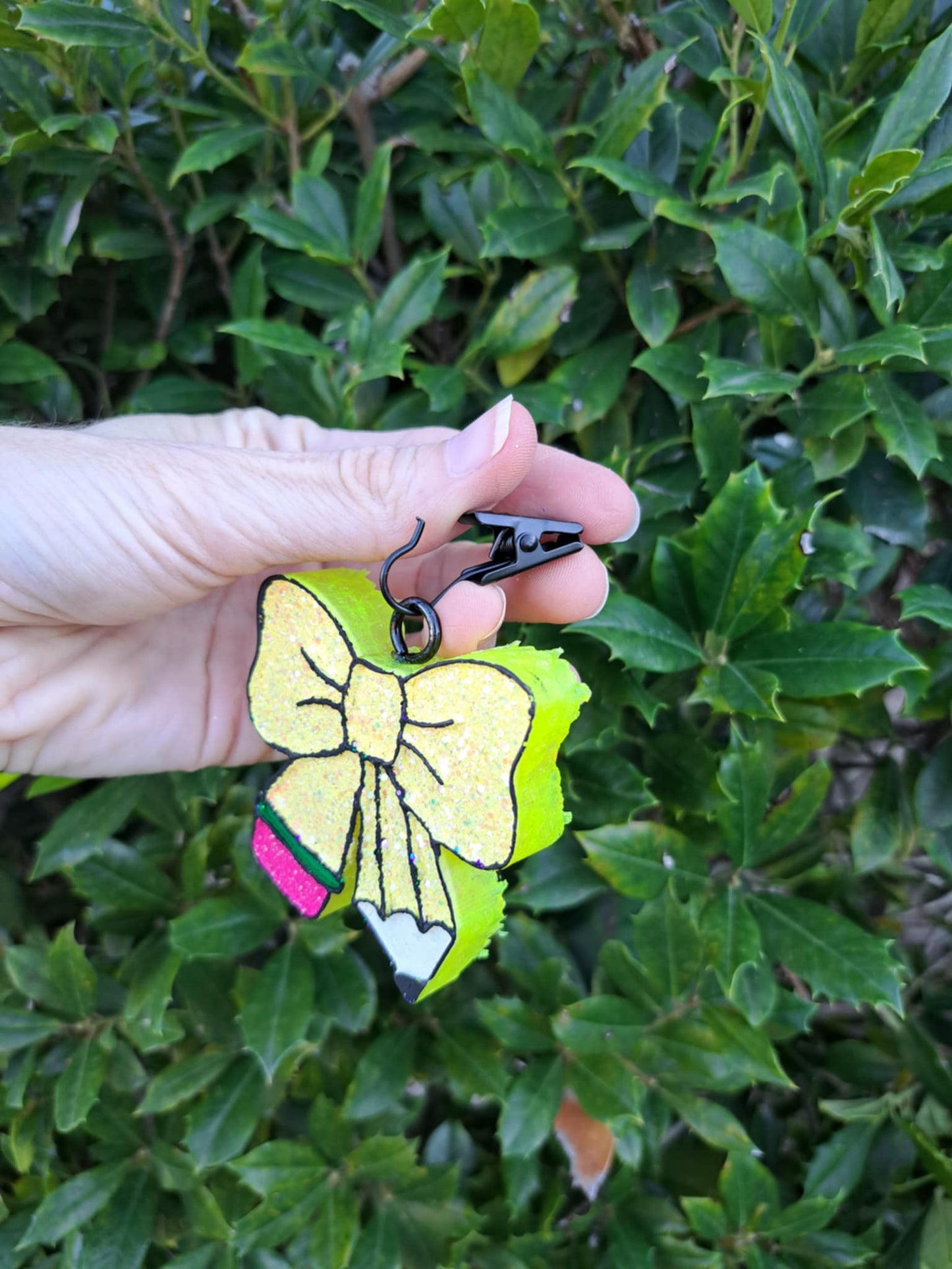 Hand holding a yellow pencil bow freshie with green leaves in the background