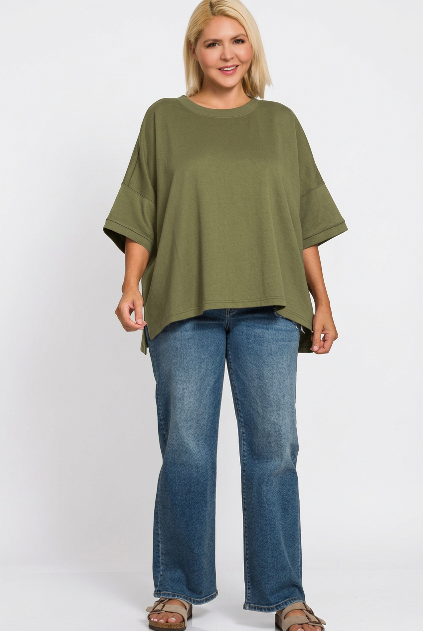woman wearing an olive loose top with jeans and sandals against a white background