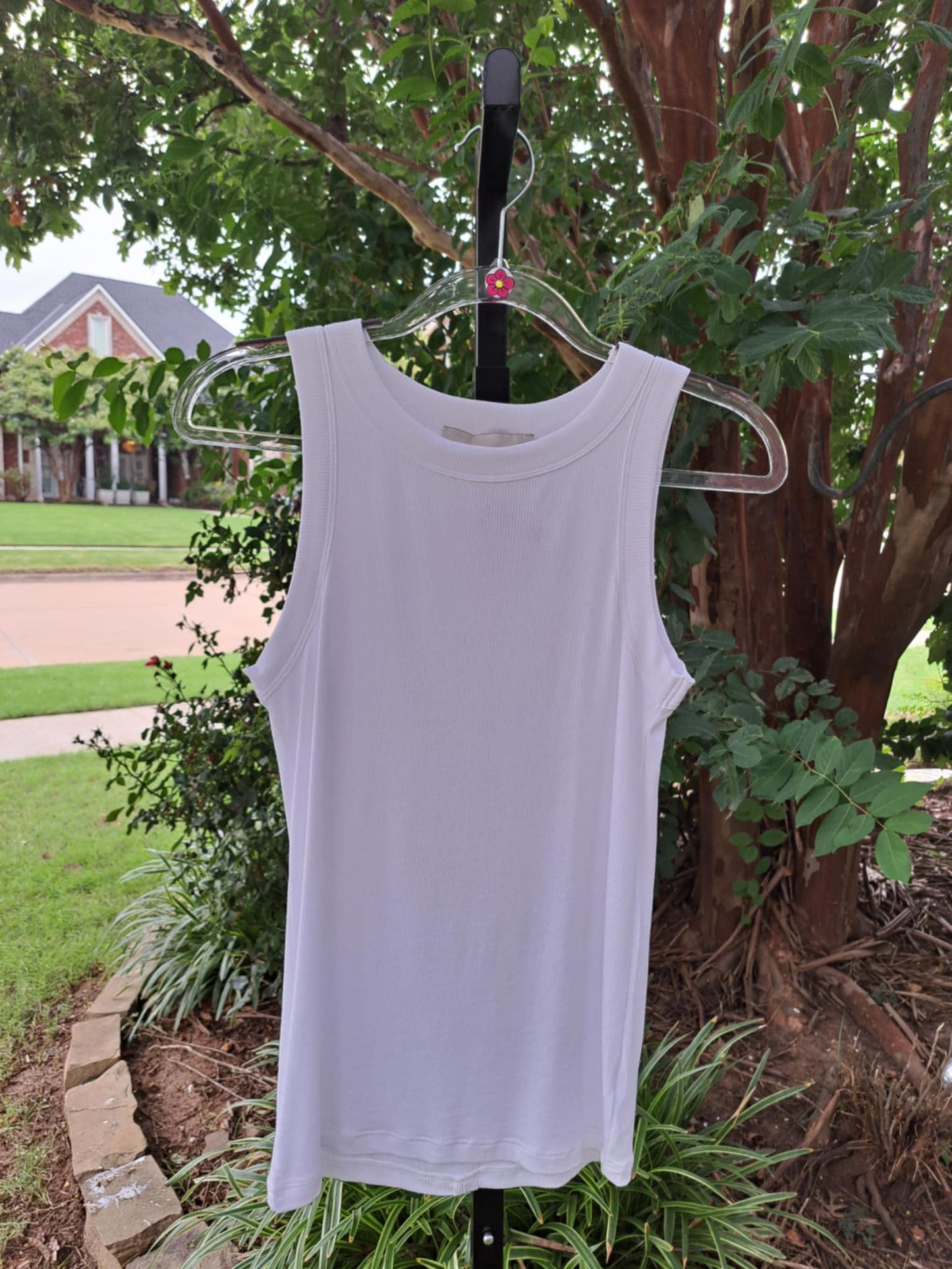 White tank top on a hanger against a natural background with trees and grass.