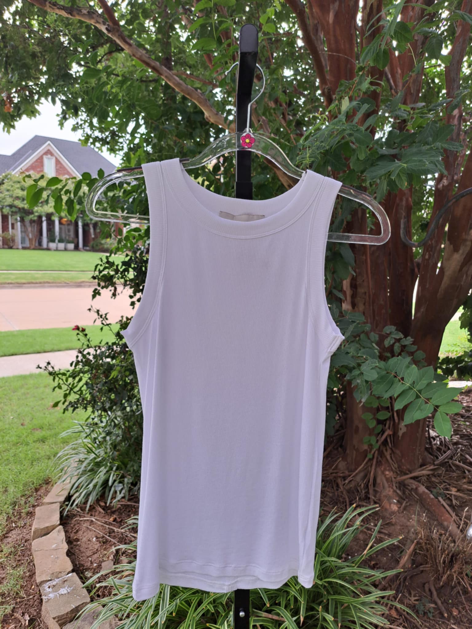 White tank top on a hanger against a natural background with trees and grass.
