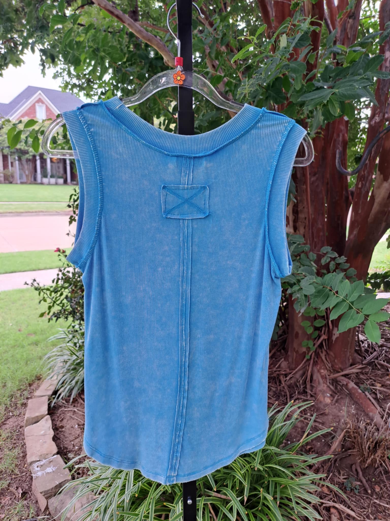 Blue sleeveless top on a hanger against a natural background with trees and grass.