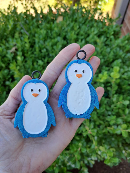 Two penguin-shaped vent clips held in a hand with a green bush background