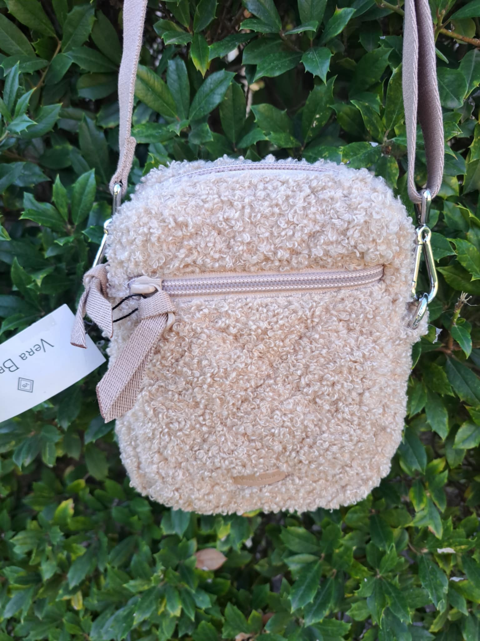 Beige textured handbag with a beige strap against a green leafy background