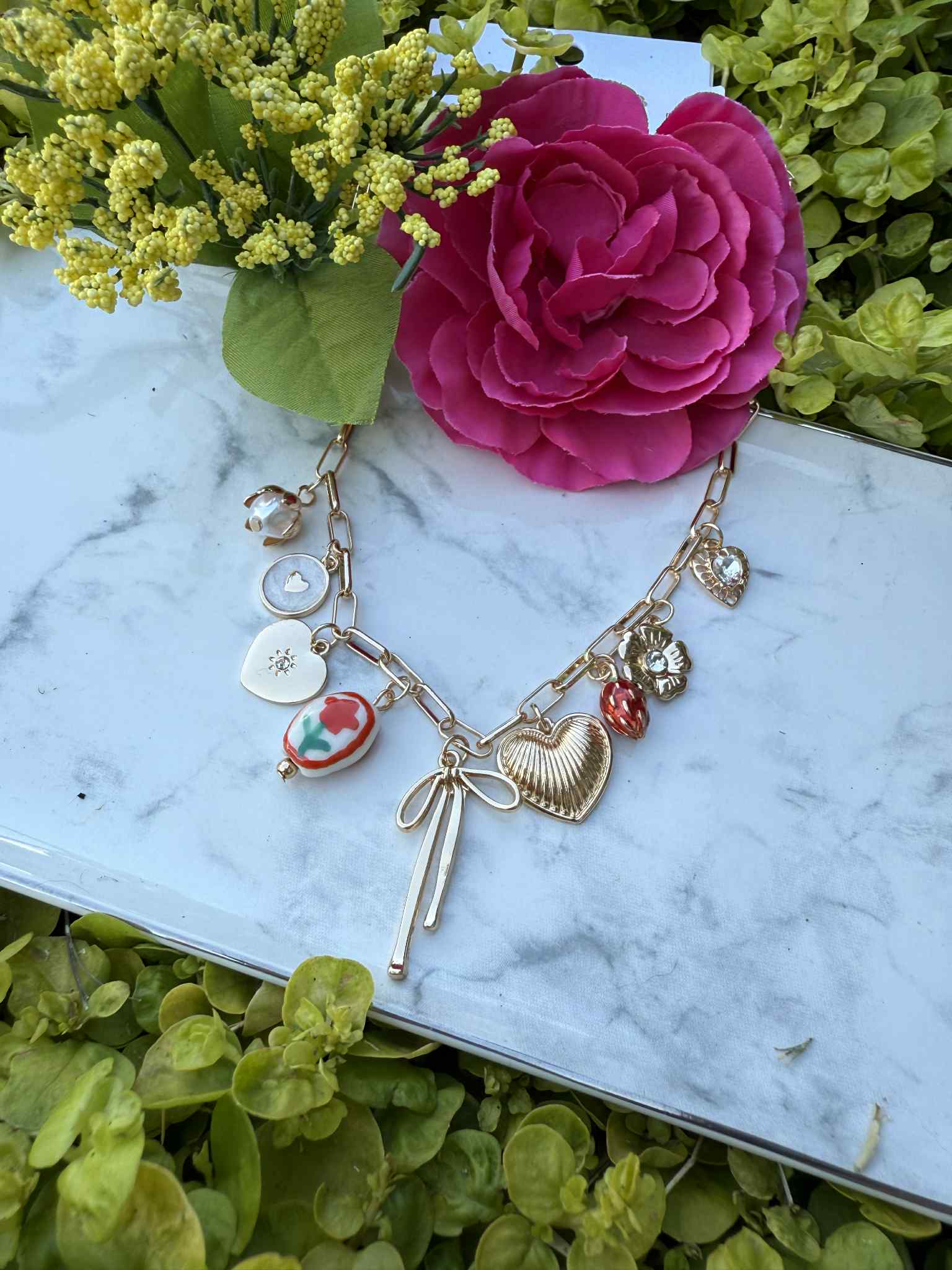Gold necklace with charms on a marble surface with flowers and greenery