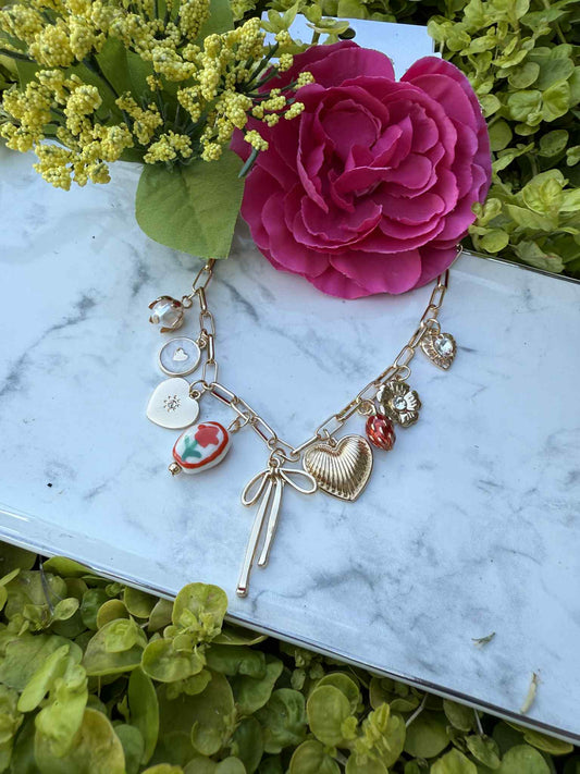 Gold necklace with charms on a marble surface with flowers and greenery