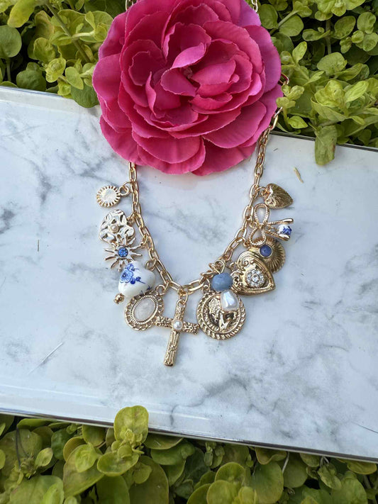 Gold necklace with charms on a marble surface with a pink flower in the background