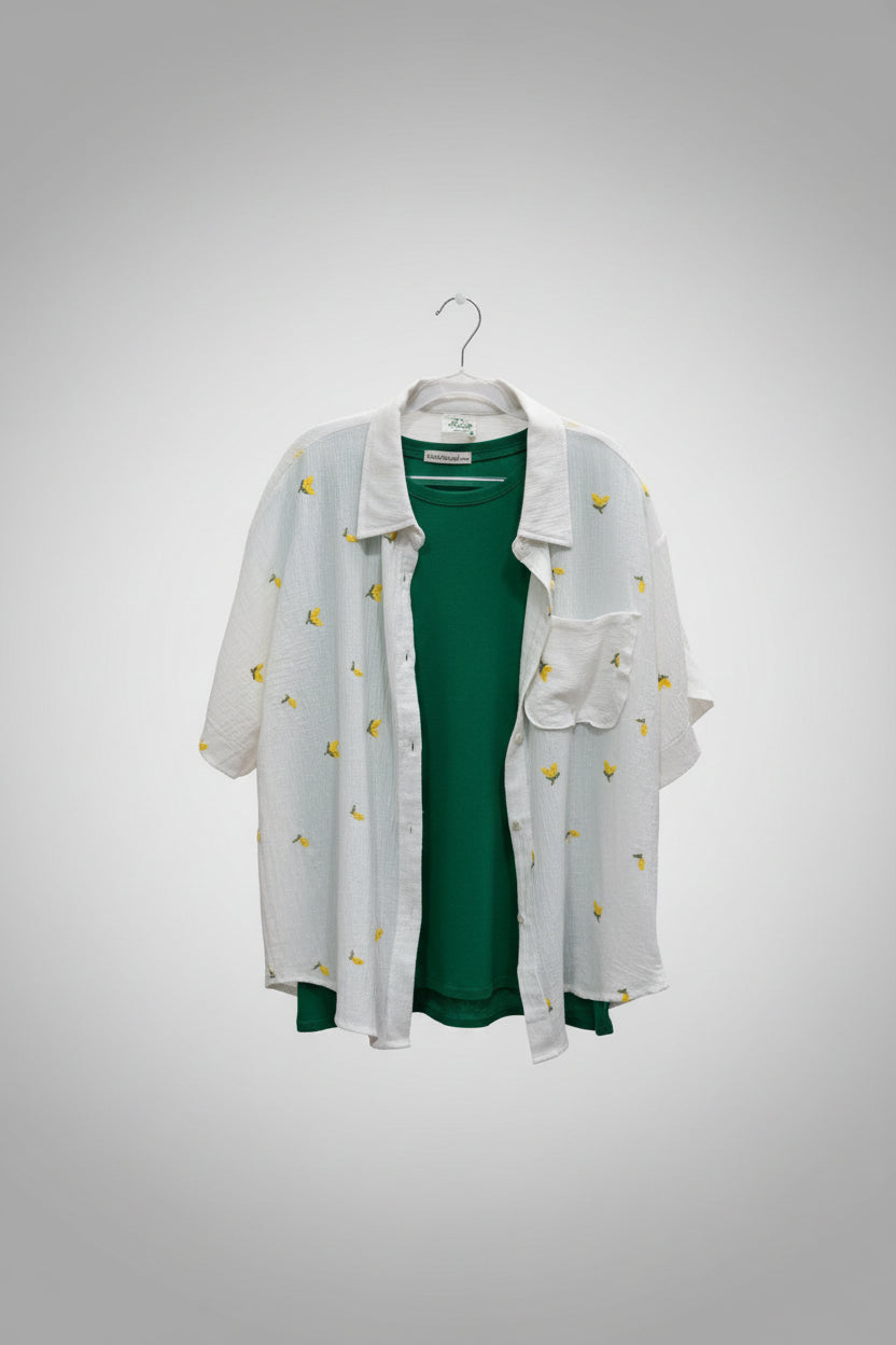 Person holding a green top with a white embroidered gauze jacket in a store setting