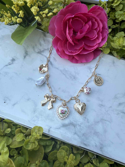 Gold necklace with charms on a marble surface with flowers