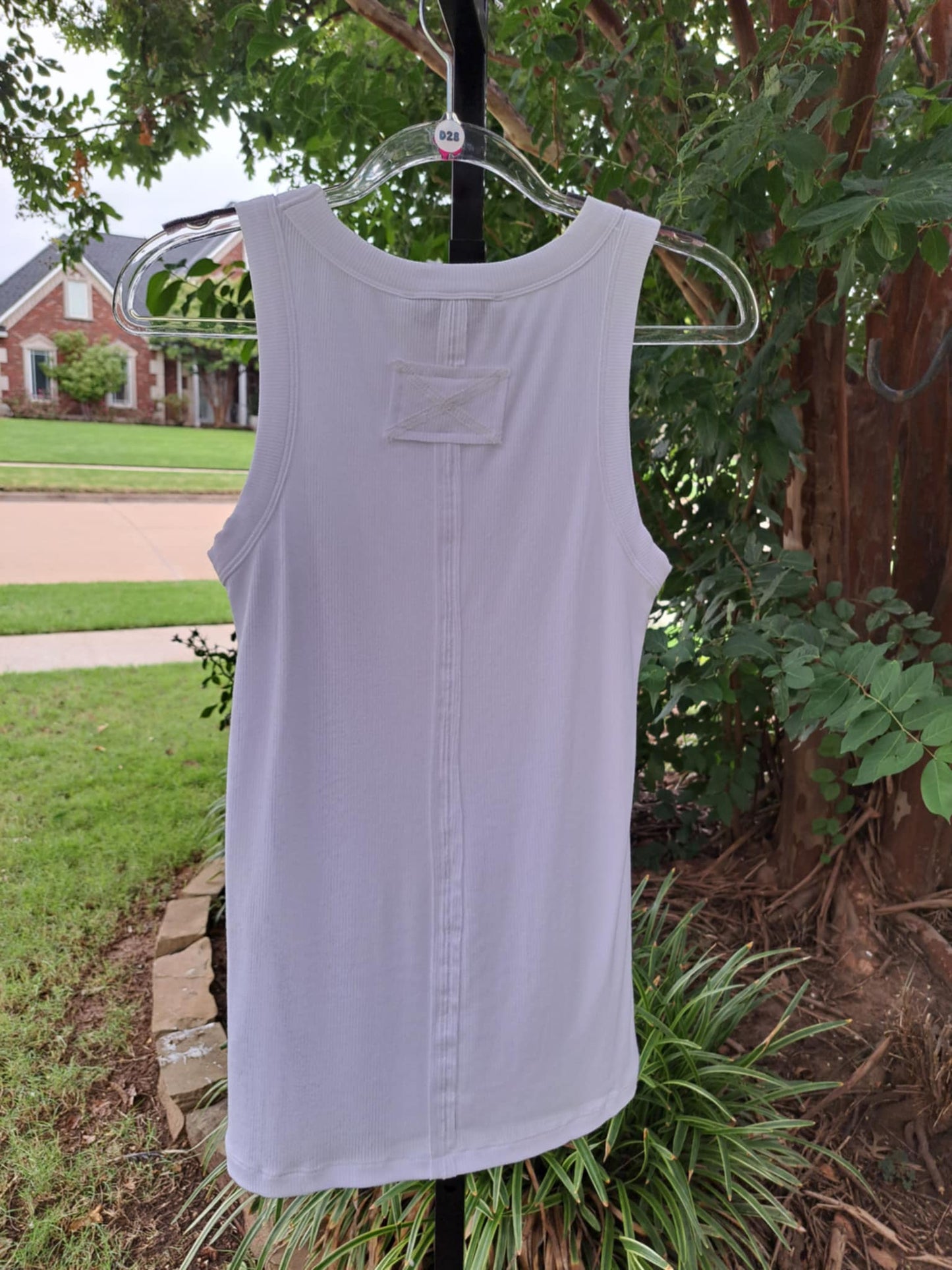 Back of a white sleeveless top on a hanger against a natural background