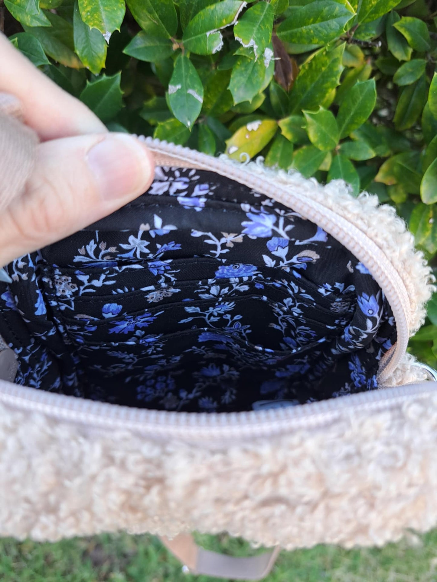 Close-up of a floral-patterned pouch with a hand holding it open, against a green leafy background.