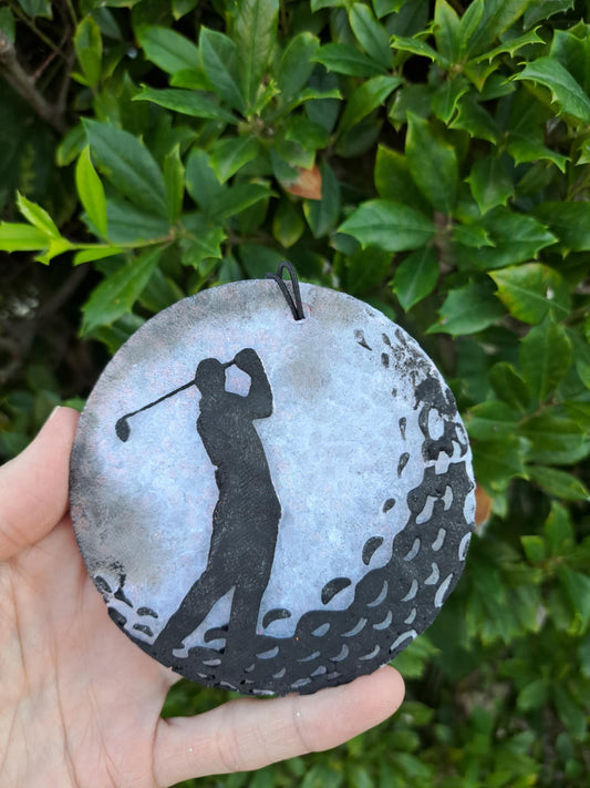 Golf ball freshie with golfer shadow design held in front of green foliage