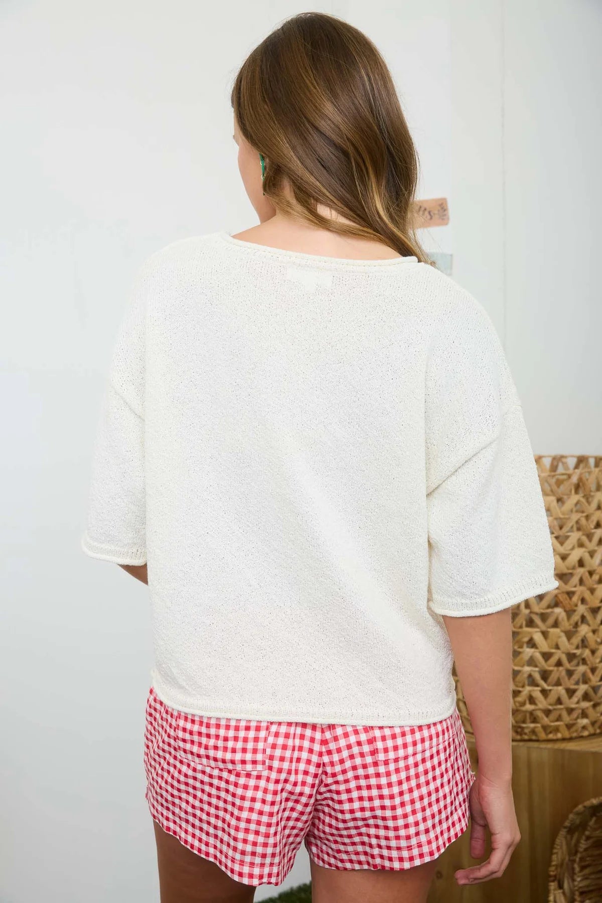 Person wearing a white oversized shirt and red checkered shorts against a plain background