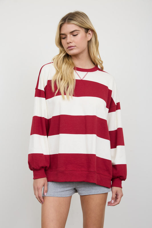 A woman wearing a red and white horizontally striped crewneck sweatshirt with balloon sleeves, paired with gray shorts, against a light gray studio background.