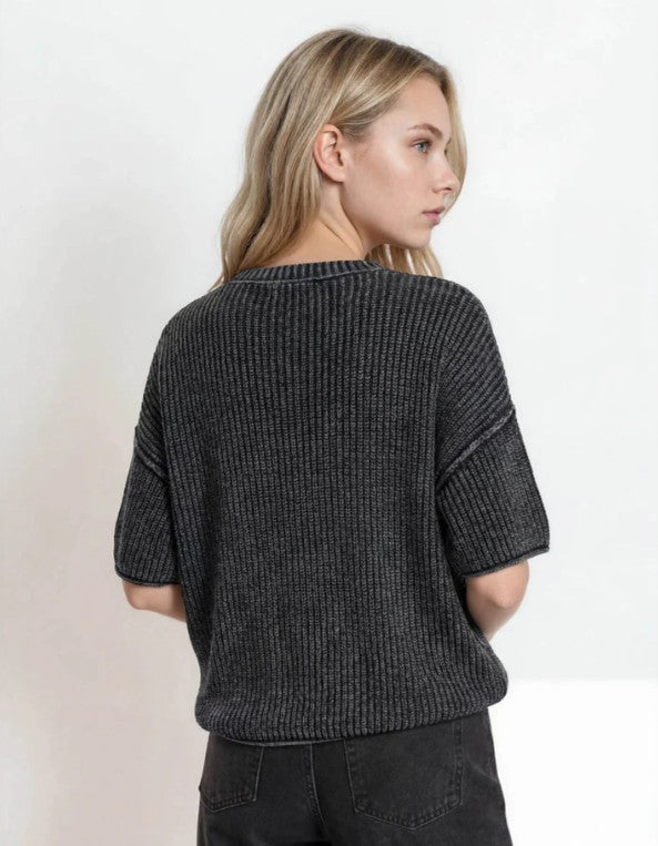 A woman shown from the back wearing a dark charcoal gray ribbed knit short-sleeve top and black jeans against a plain white studio background.
