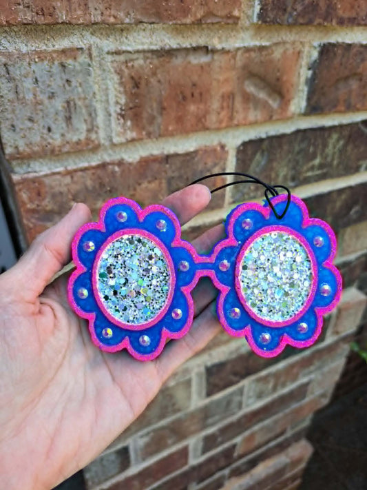 Blue and pink glitter glasses freshie held in front of brick wall