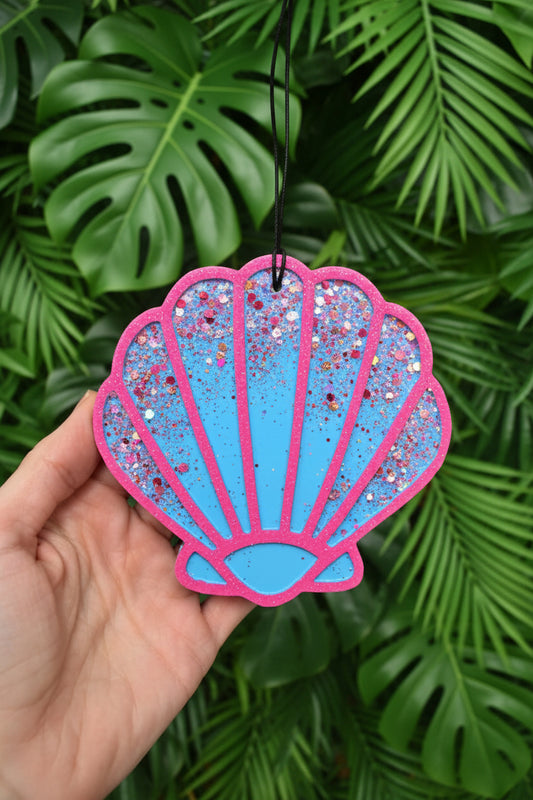 Seashell-shaped decorative item with pink and blue gradient and glittery texture, held against a dark background.