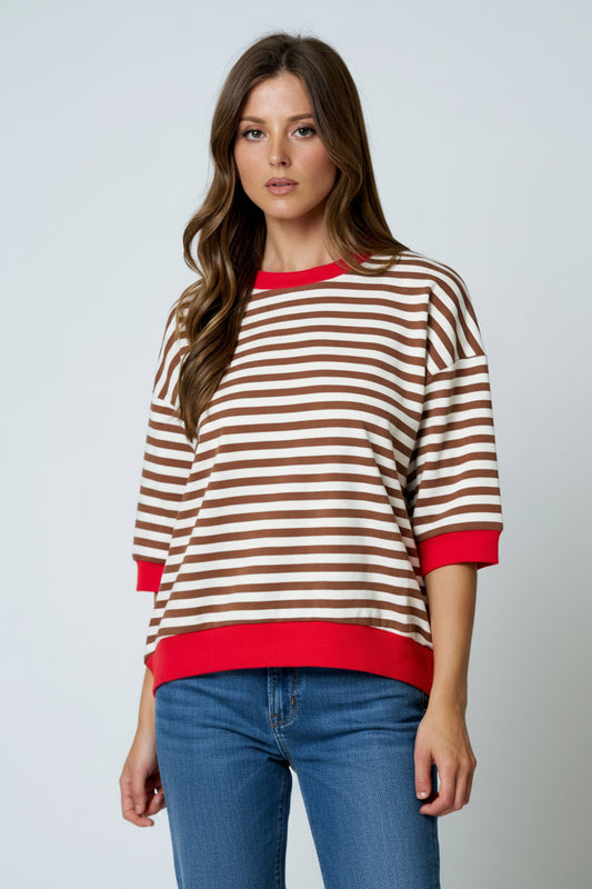 Woman wearing a brown and red striped sweater with blue jeans on a gray background