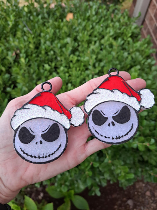 Two decorative skull vent clips with Santa hats held in front of a green bush.