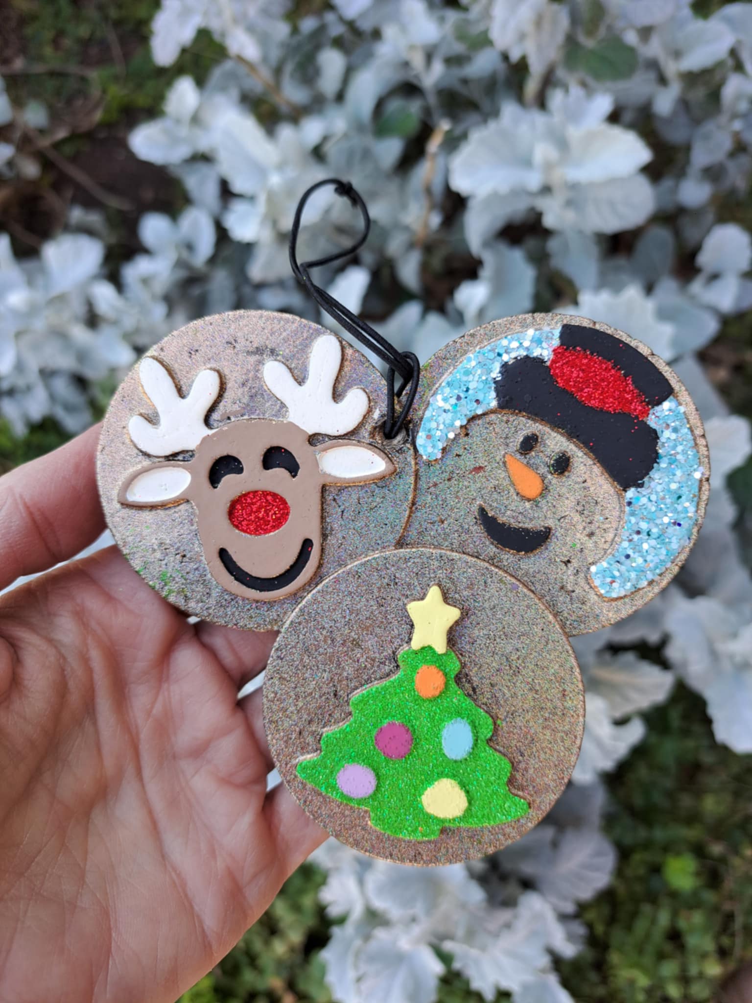 Christmas cookie freshie with deer tree and snowman held by a hand on a background of greenery