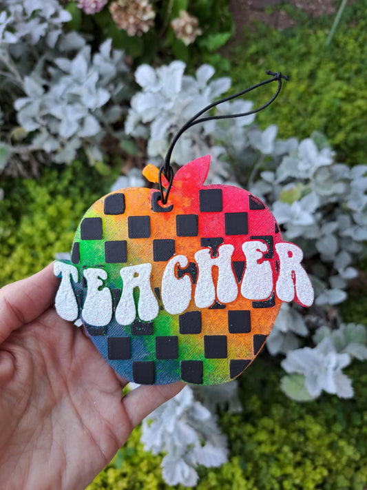 Colorful checkered apple that says "TEAHCER" held in front of greenry