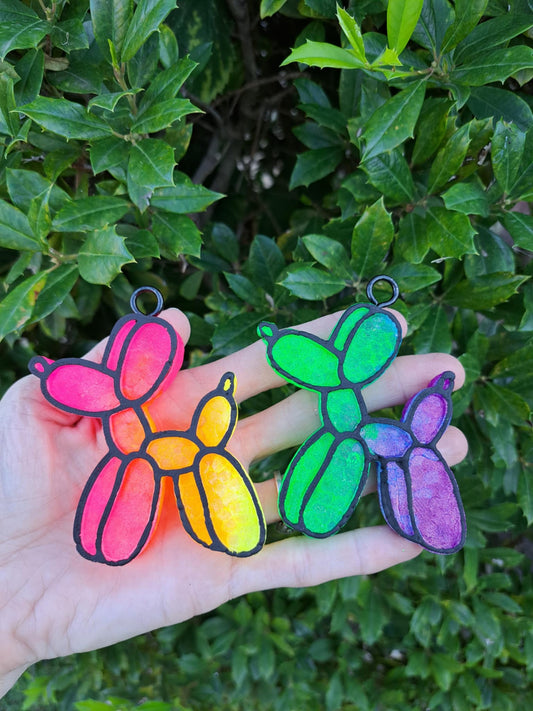 colorful balloon dog vent clips in hand in front of greenry background