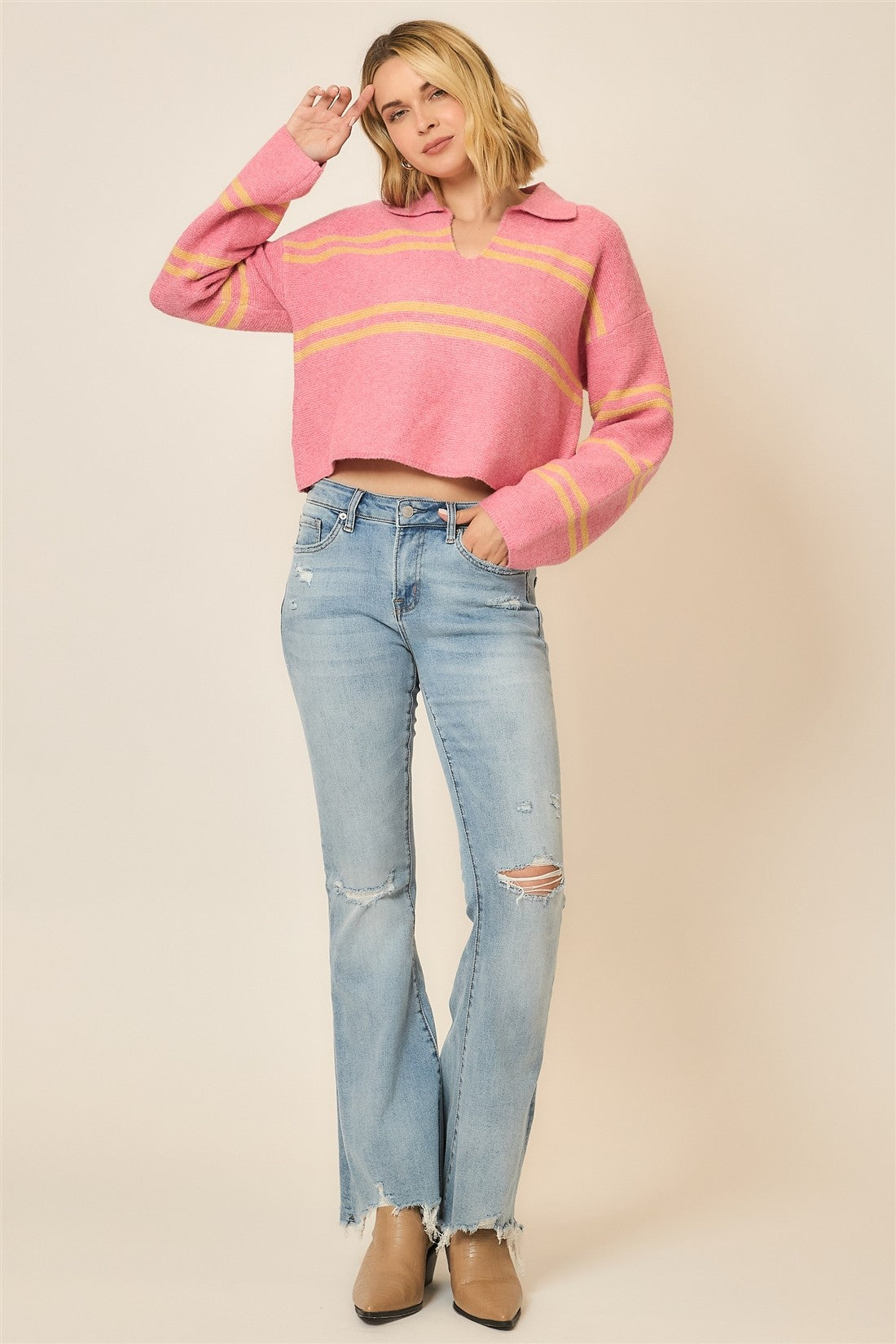 woman wearing a pink vneck sweater with orange stripes, distressed jeans, and an boots on a neutral background