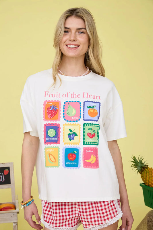 Woman wearing a white t-shirt with colorful fruit graphics and red shorts on a yellow background
