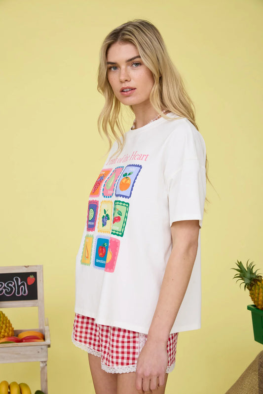 Woman wearing a white t-shirt with colorful fruit graphics and red checkered shorts on a yellow background.