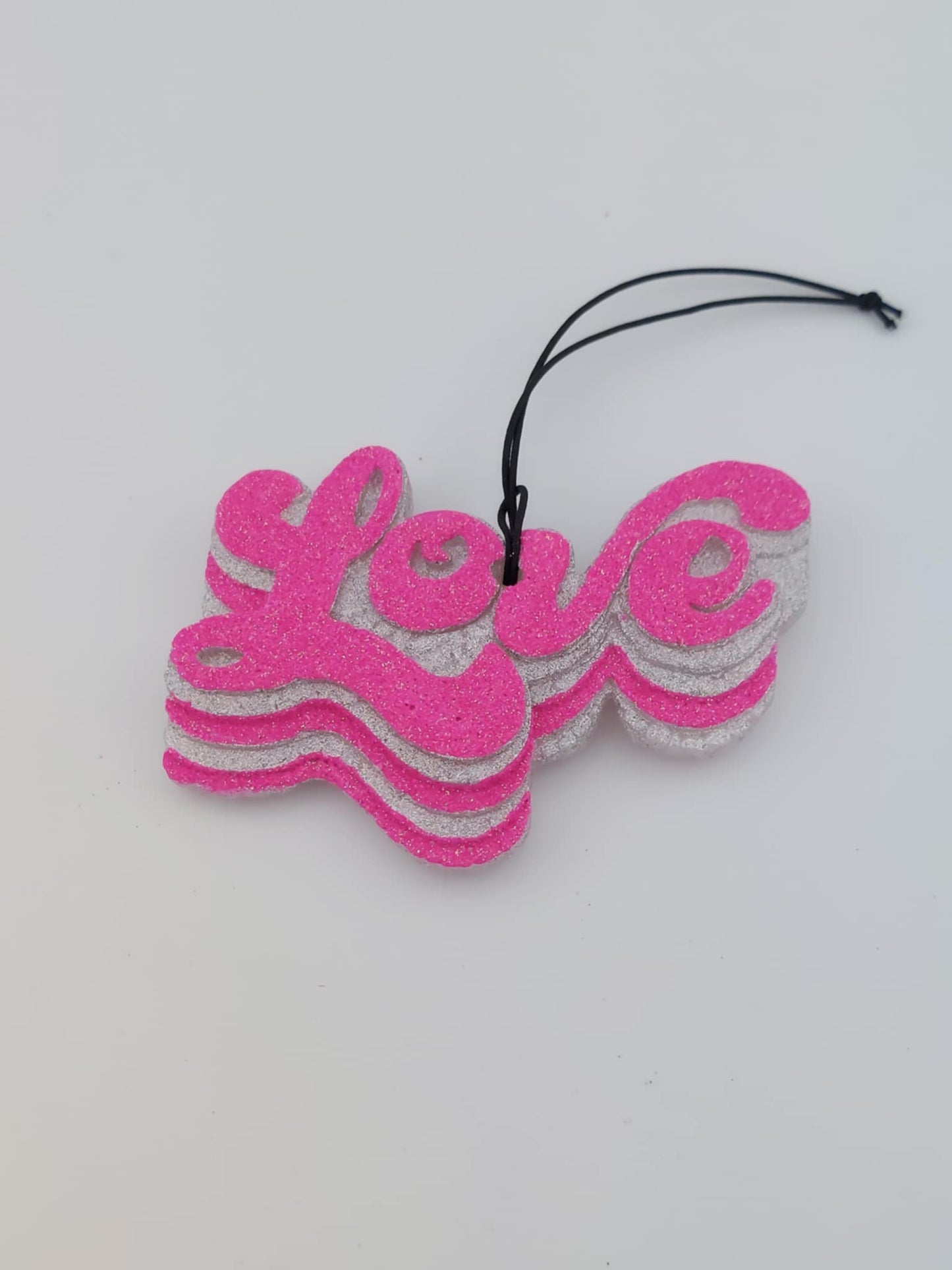 A pink 'Love' script air freshener with black elastic string for hanging