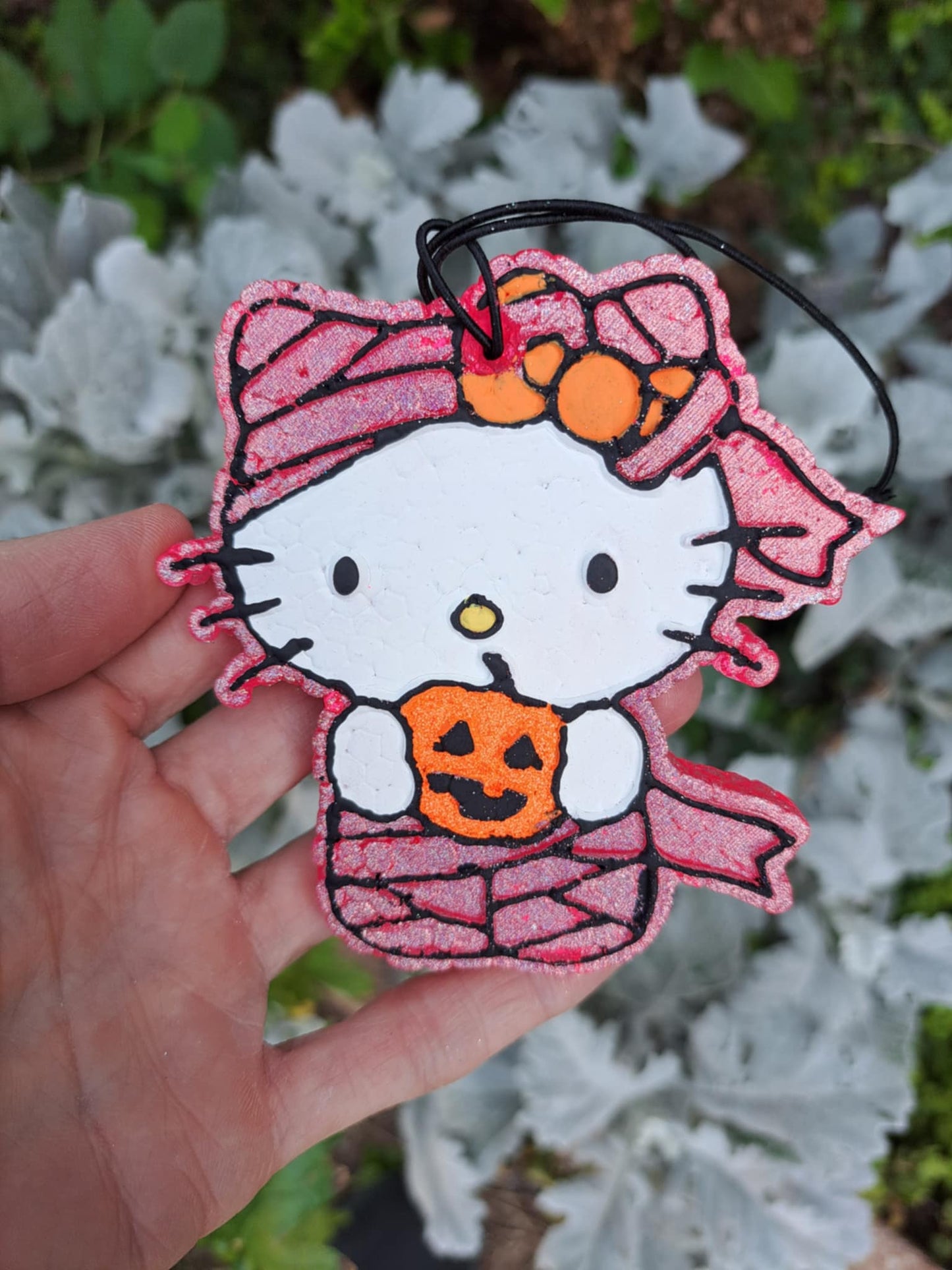 Mummy kitty holding pumpkin air freshener held by a hand with a blurred natural background