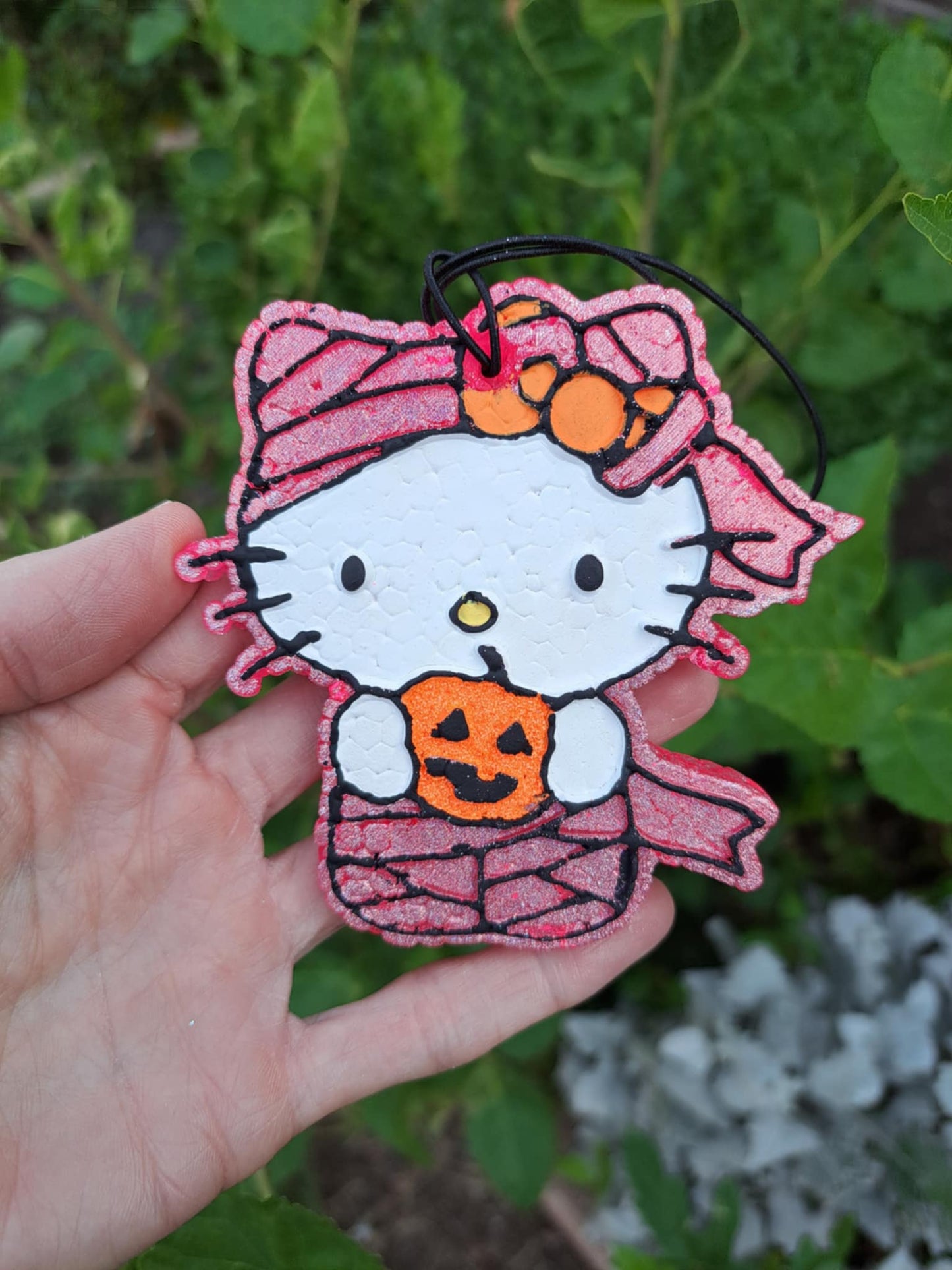 Mummy kitty holding pumpkin. Held by hand in front of foilage.