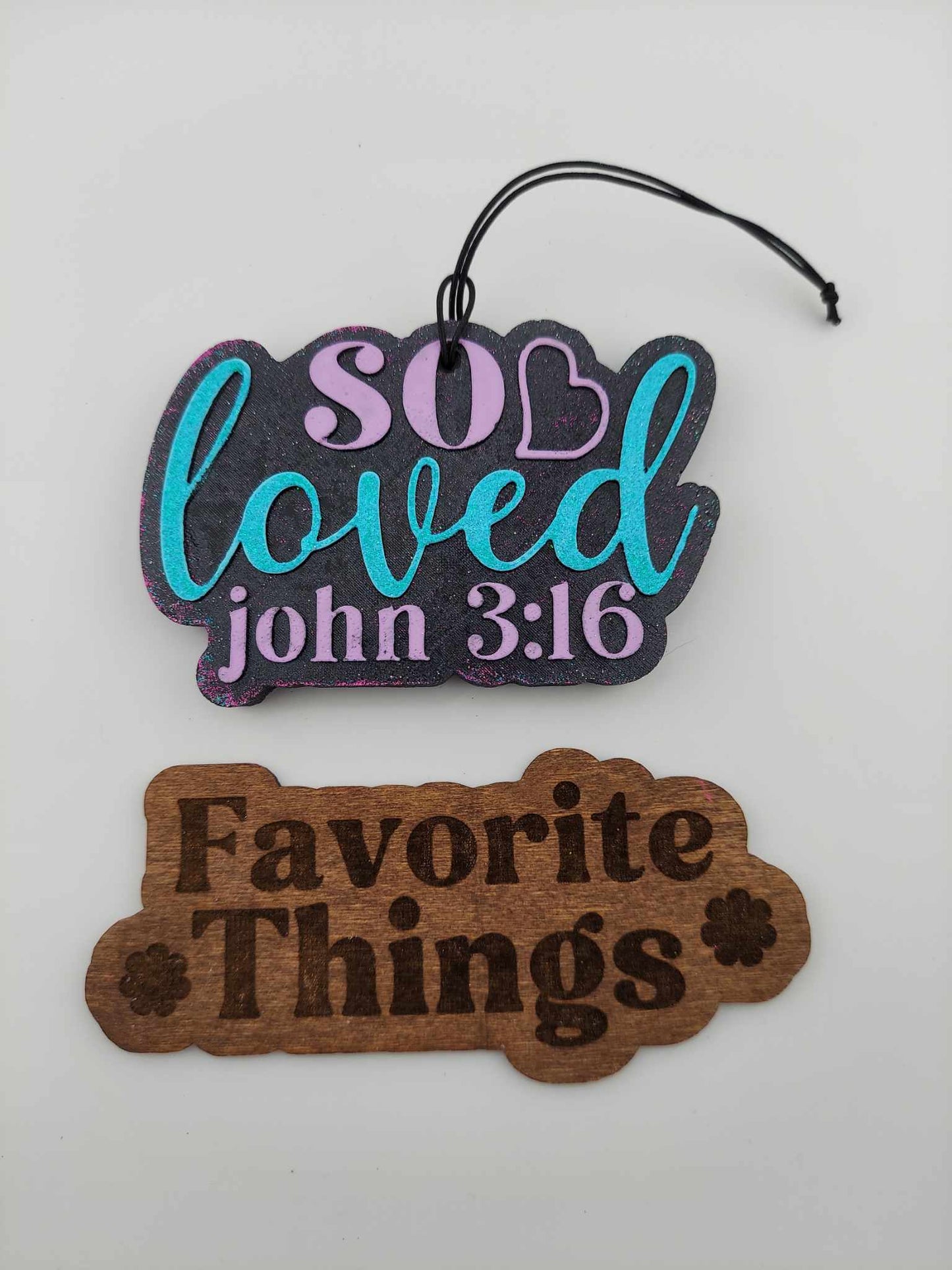 Handmade air freshener that says 'So Loved' in multicolored lettering on a white background. Below is a brown 'Favorite Things' wooden sign
