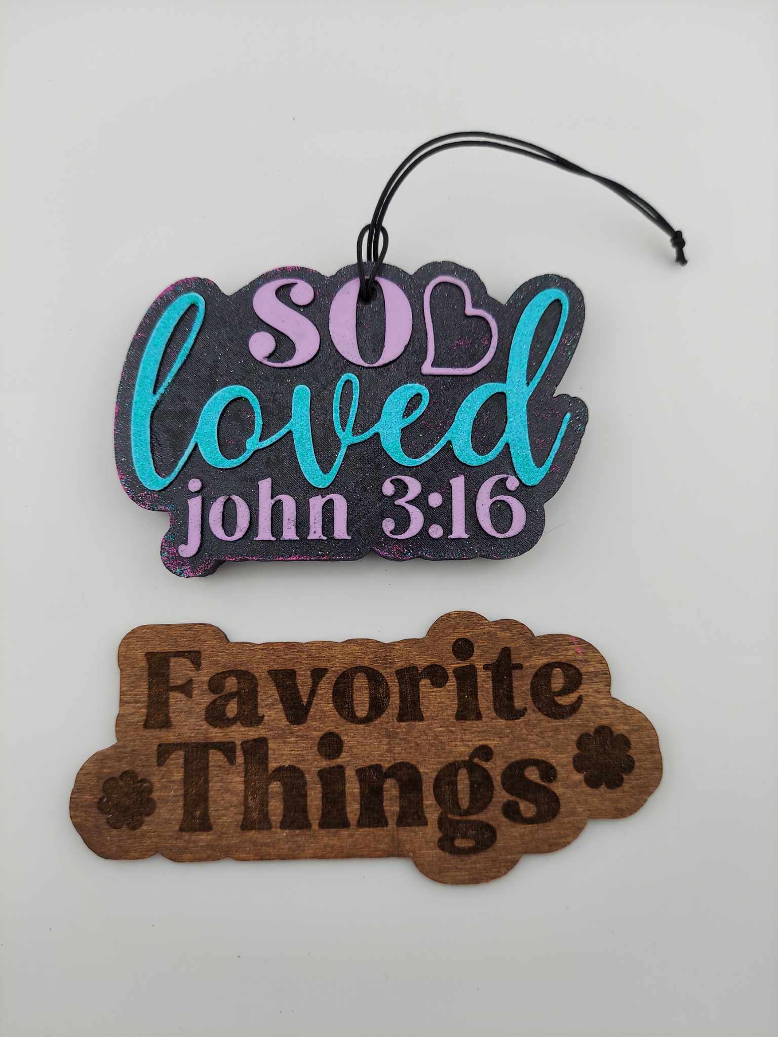 Handmade air freshener that says 'So Loved' in multicolored lettering on a white background. Below is a brown 'Favorite Things' wooden sign