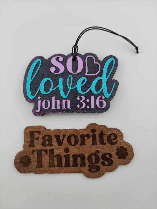Handmade air freshener that says 'So Loved' in multicolored lettering on a white background. Below is a brown 'Favorite Things' wooden sign