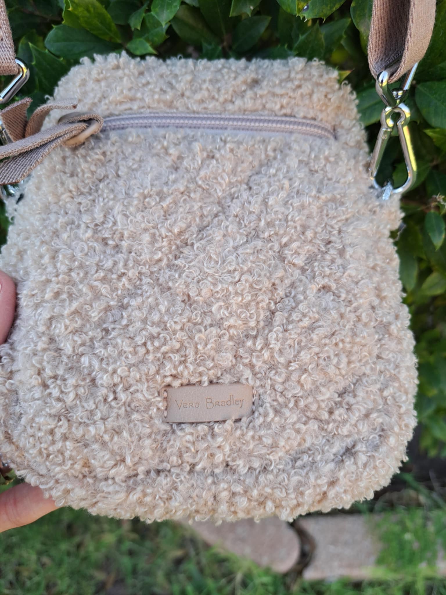 Beige textured handbag held against a green leafy background. Says Vera Bradley