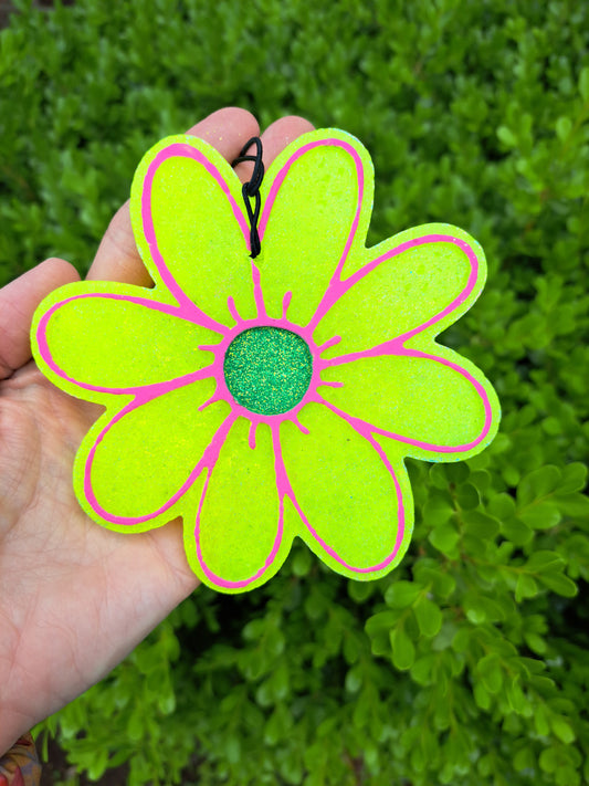Hand holding a yellow daisy freshie with pink outline against a green leafy background