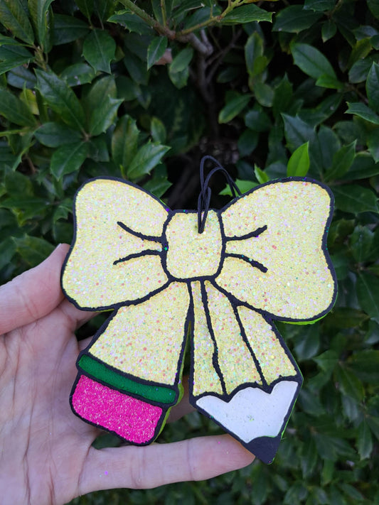 Yellow glitter pencil bow freshie held against a green leafy background