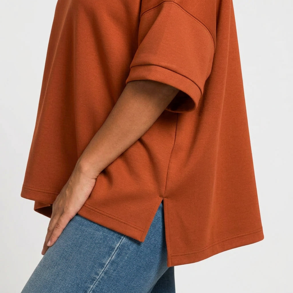 Close-up of a person wearing an oversized brown short-sleeve top with blue jeans, cropped to show the side and back drape of the shirt.