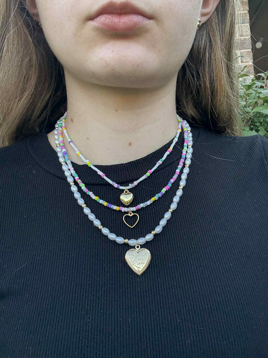 Person wearing multiple necklaces with heart pendants on a black shirt.