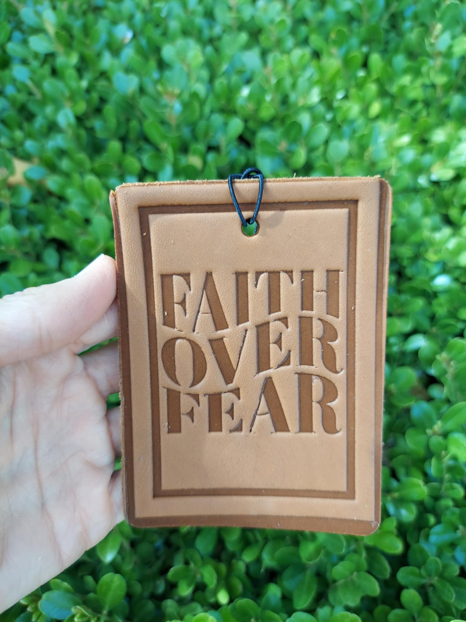Brown leather tag with 'Faith Over Fear' text held against a green grass background