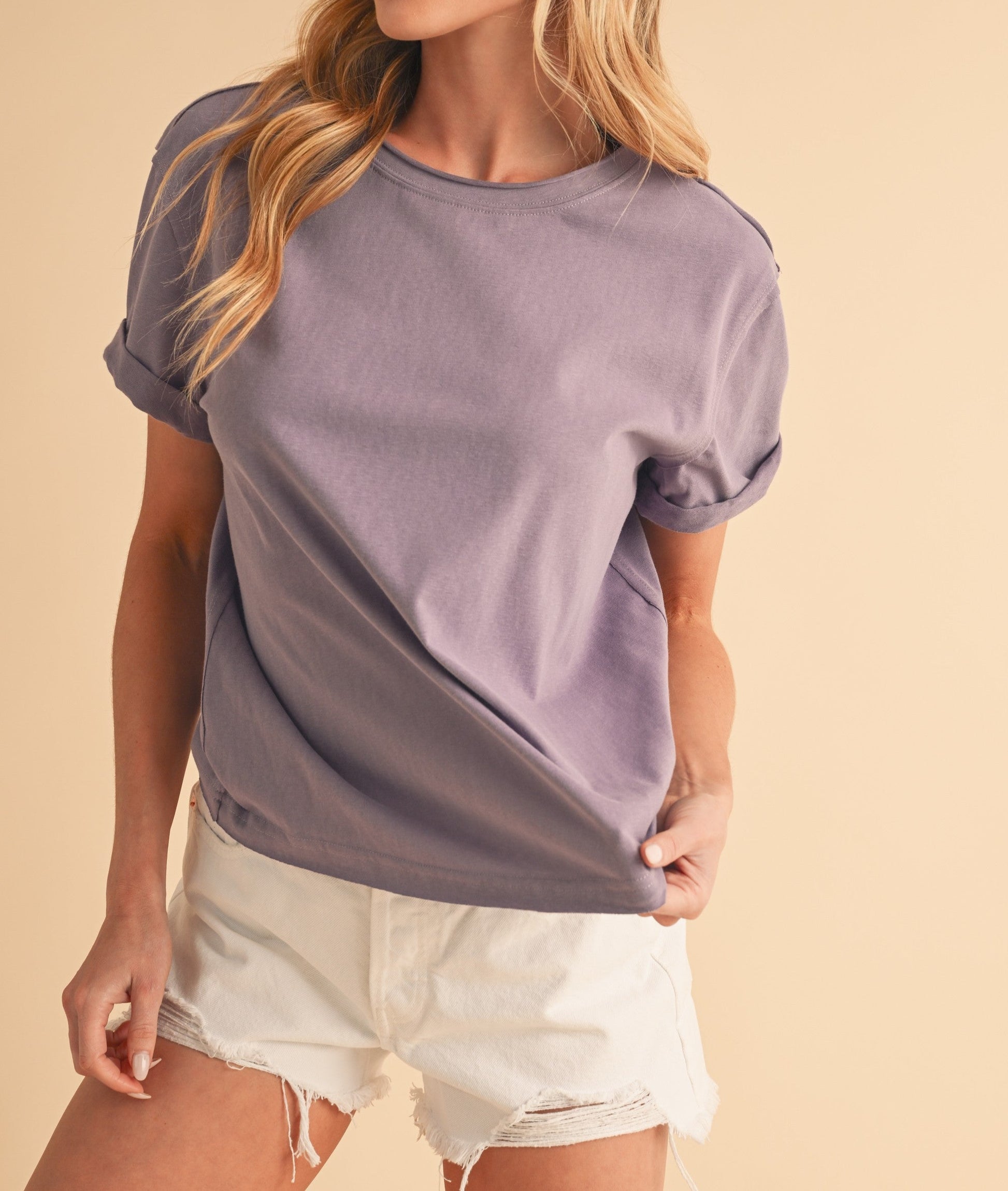 Woman wearing a purple t-shirt and white shorts on a beige background