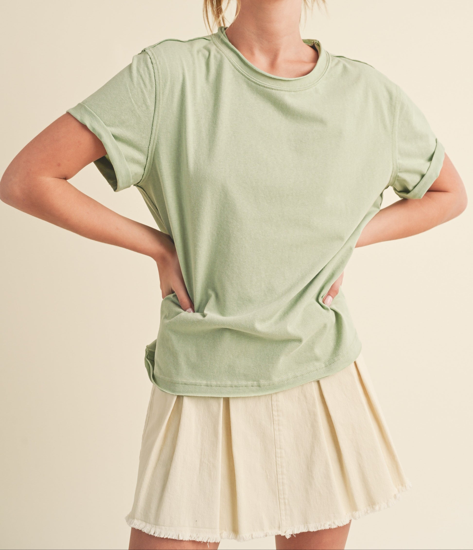 Woman wearing a light green oversized t-shirt and beige skirt on a beige background