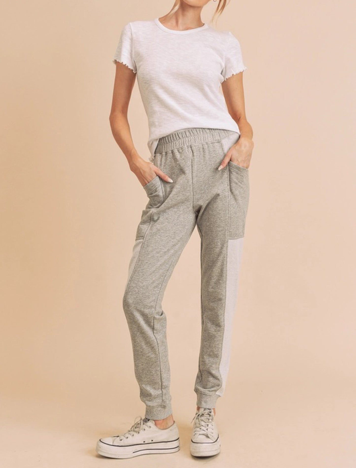 Woman wearing a white t-shirt and gray jogger pants on a beige background
