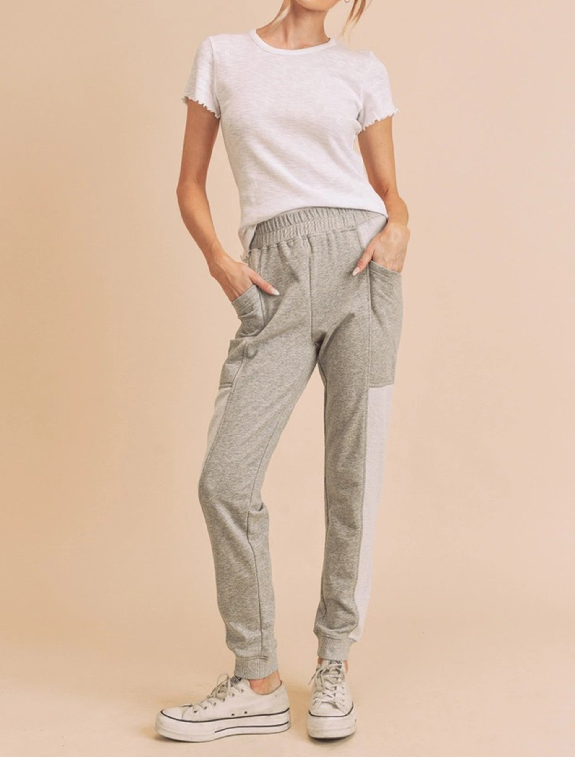 Woman wearing a white t-shirt and gray jogger pants on a beige background
