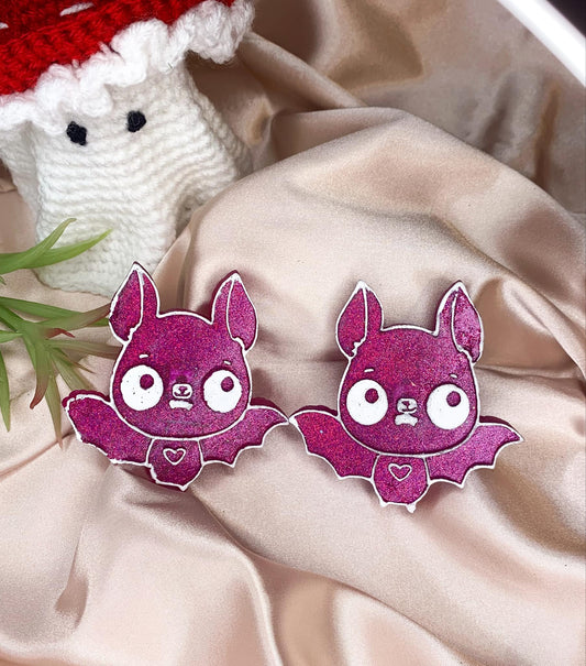 Two purple bat shaped vent clips on a beige silk background with ghost in the corner.