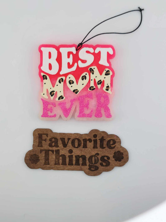 A handmade, painted hanging air freshener with 'BEST MOM EVER' text in pink, decorated with a leopard print design, and a separate brown tag reading 'Favorite Things'.
